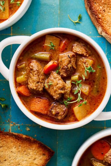 slow cooker beef stew in a white bowl with bread on the side