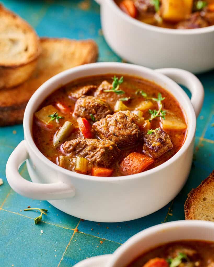slow cooker beef stew in a white bowl with bread on the side
