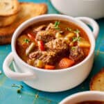 slow cooker beef stew in a white bowl with bread on the side