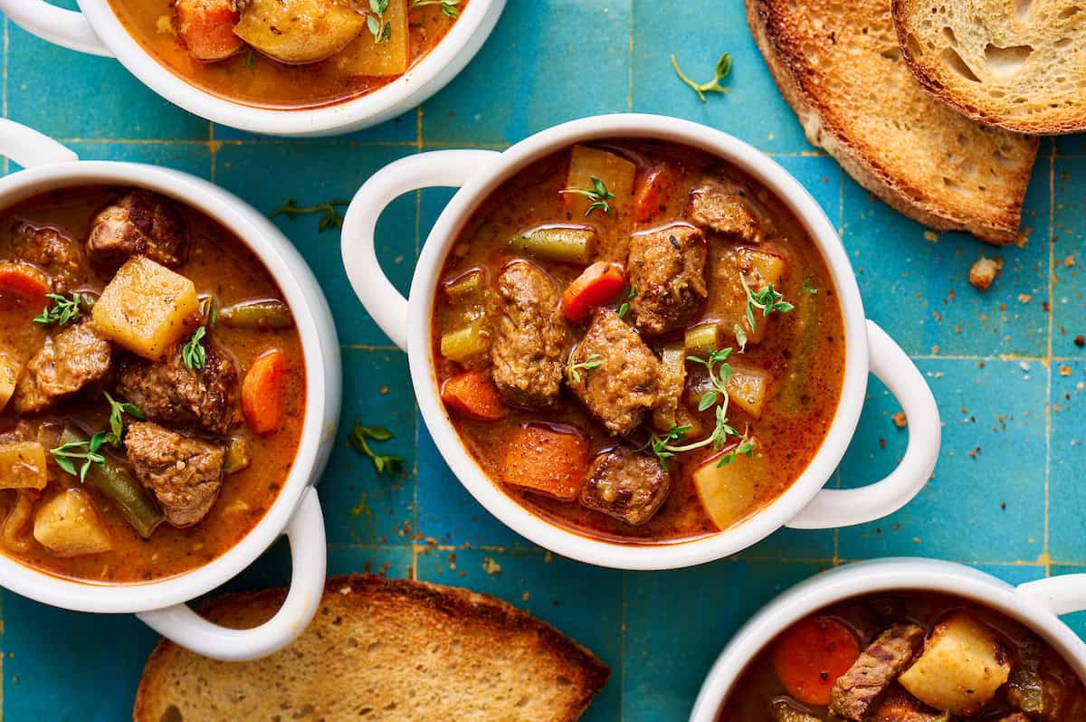 slow cooker beef stew in white bowls with bread on the side