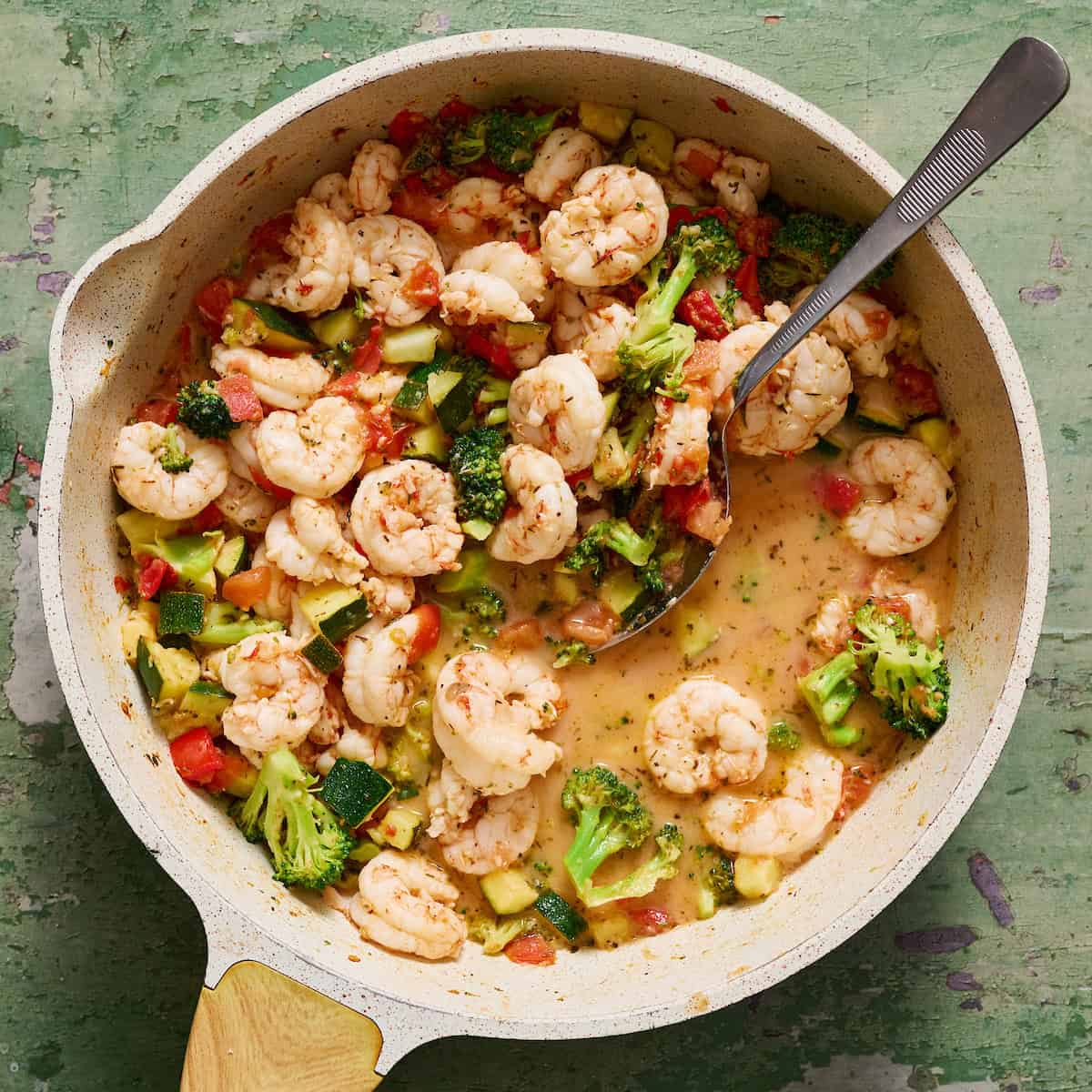 shrimp and vegetables in a pan with the sauce created and visible with a spoon
