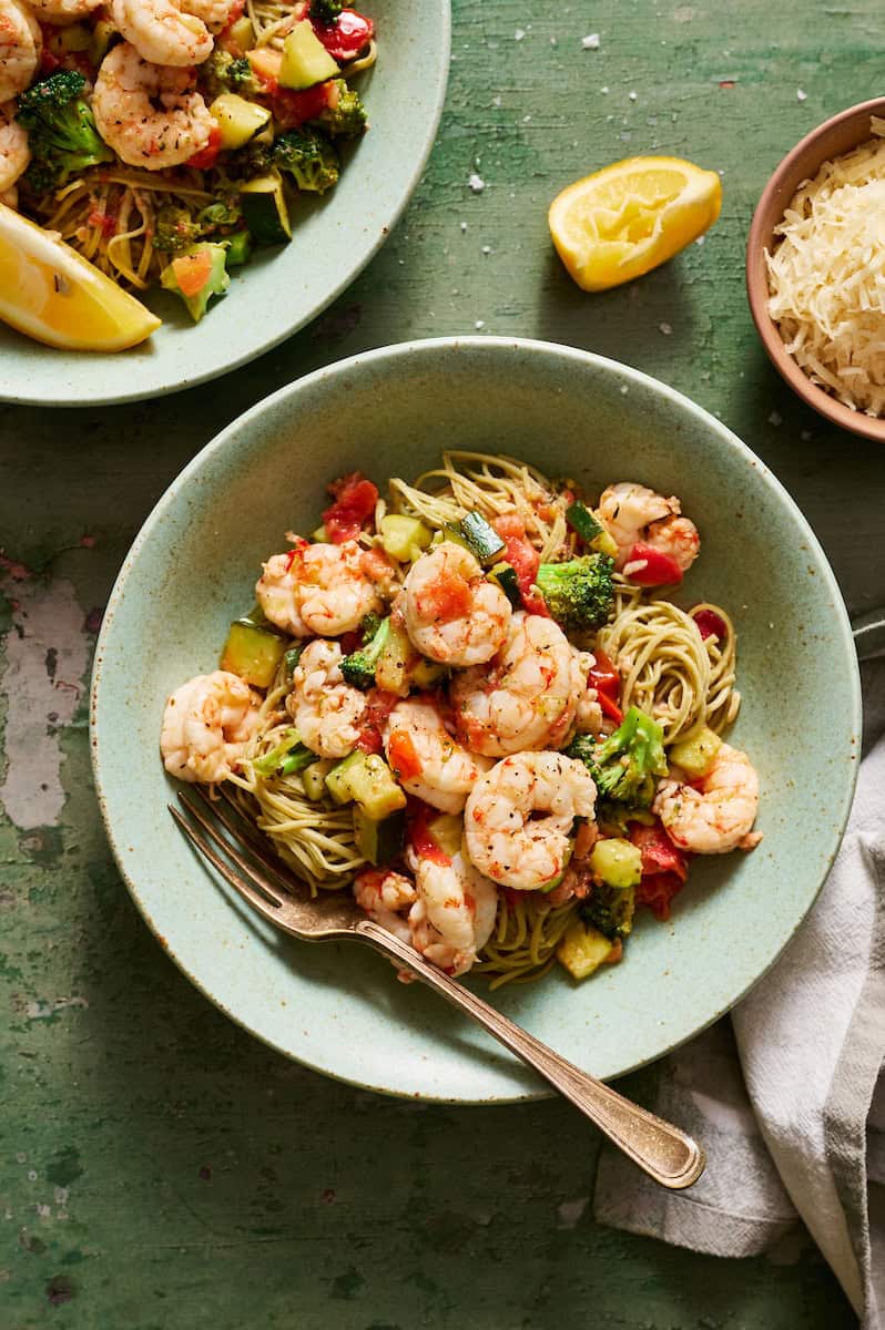 Veggie shrimp pasta plated in bowls with extra lemon and parmesan on the side