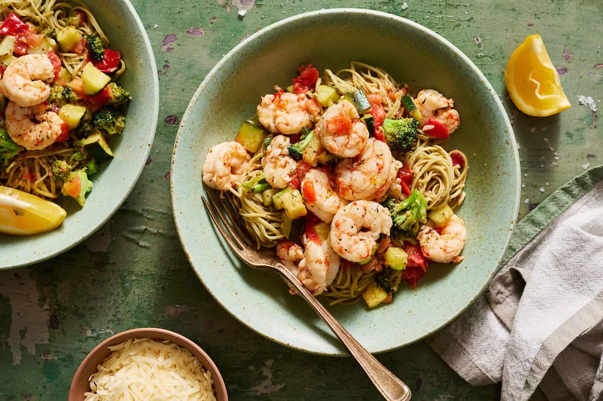 Veggie shrimp pasta plated in bowls with extra lemon and parmesan on the side