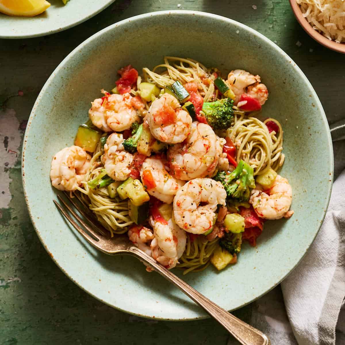 Veggie shrimp pasta plated in bowls with extra lemon and parmesan on the side