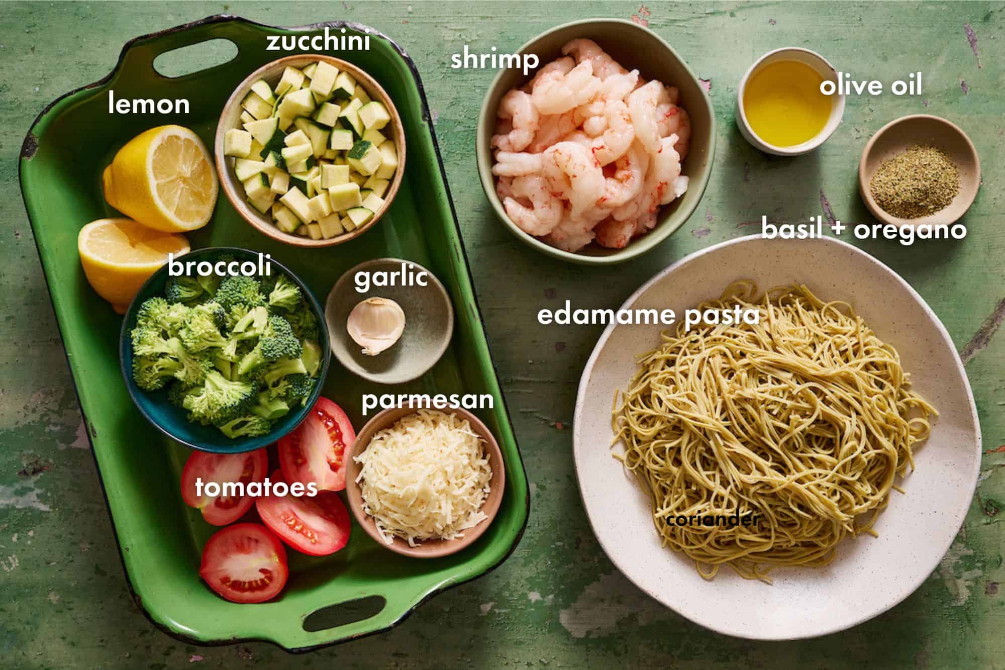 ingredients laid out to make veggie shrimp pasta including garlic, broccoli, tomatoes, lemon, zucchini, olive oil and spices