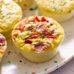 whole egg bite on a plate with red peppers, chives and bacon