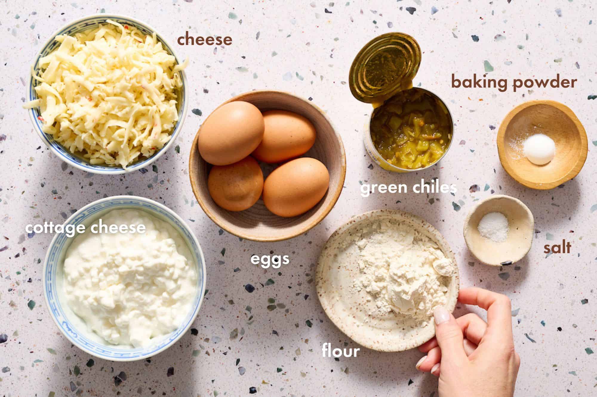 ingredients for making egg bites including eggs, cottage cheese, shredded cheese, flour, baking powder, green chiles and salt