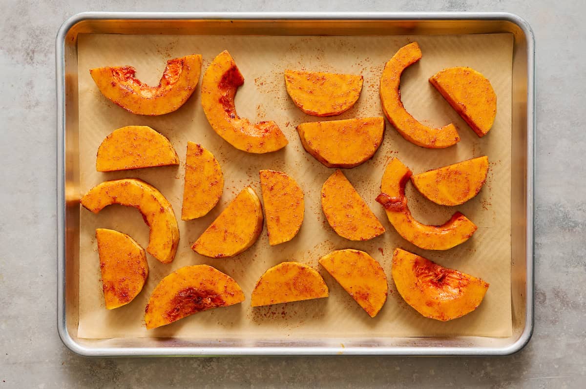 butternut squash tossed in spices and olive oil ready to be baked on a sheet tray with parchment paper
