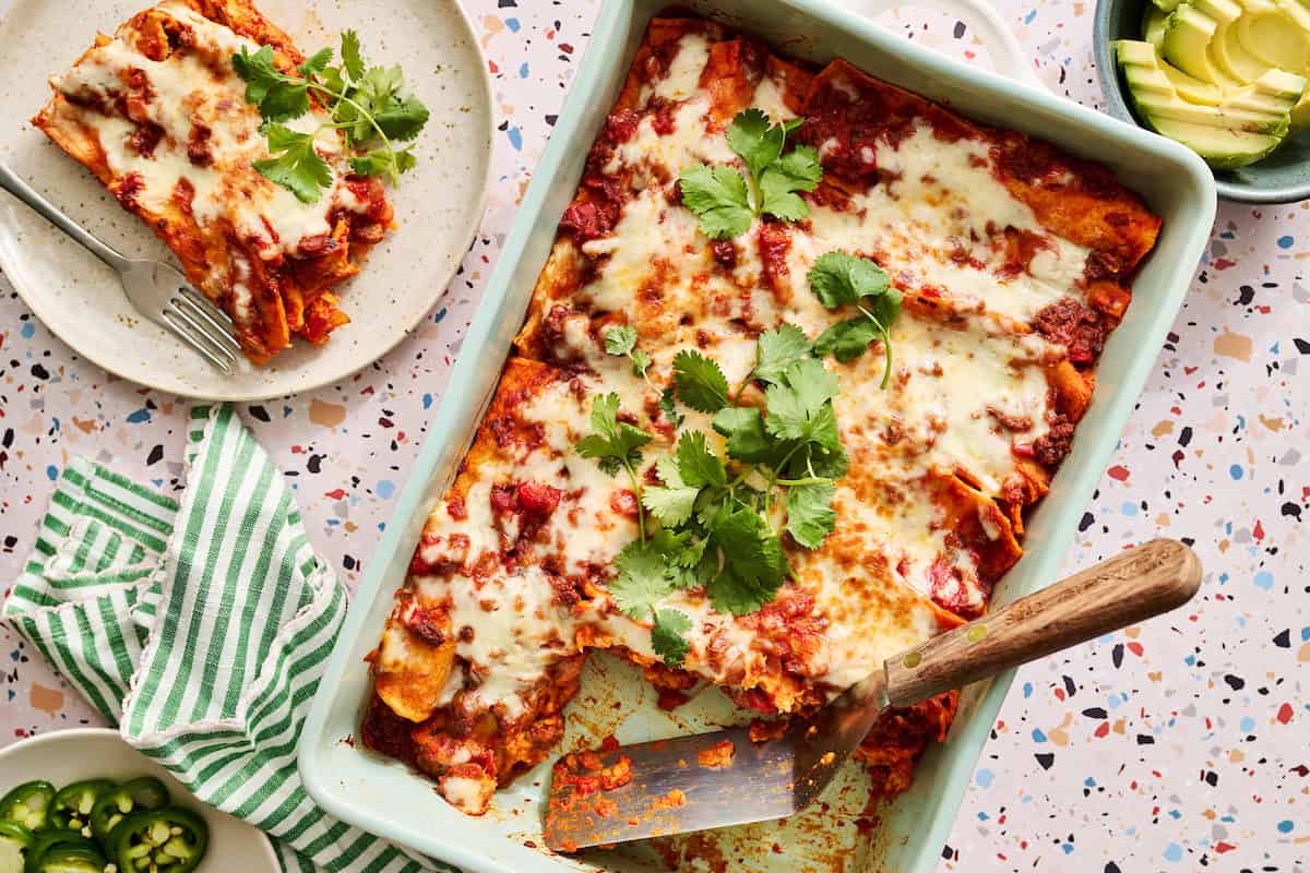 Ground Beef Enchiladas with a serving removed and plated along with fresh jalapenos and avocado