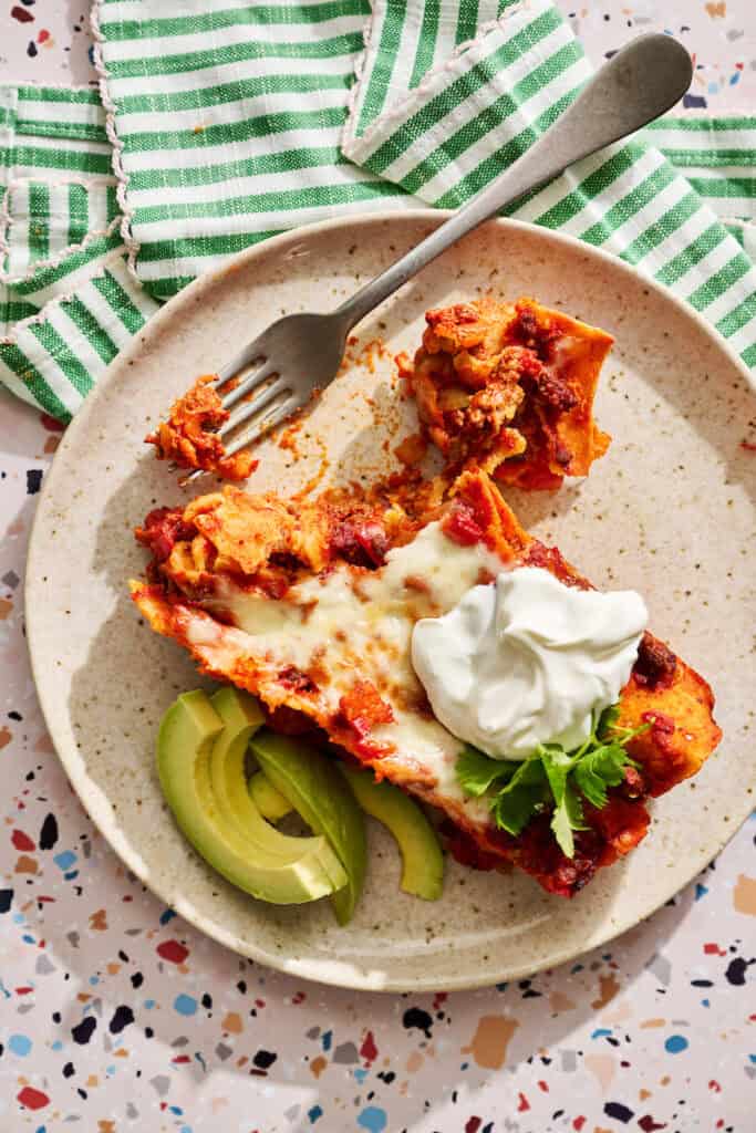 Ground Beef Enchiladas single serving on a plate with sour cream and avocado