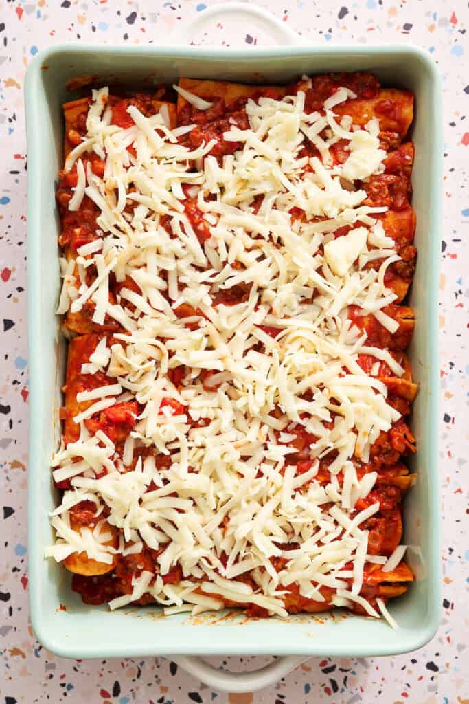 enchiladas in the process of being made right after shredded cheese is added