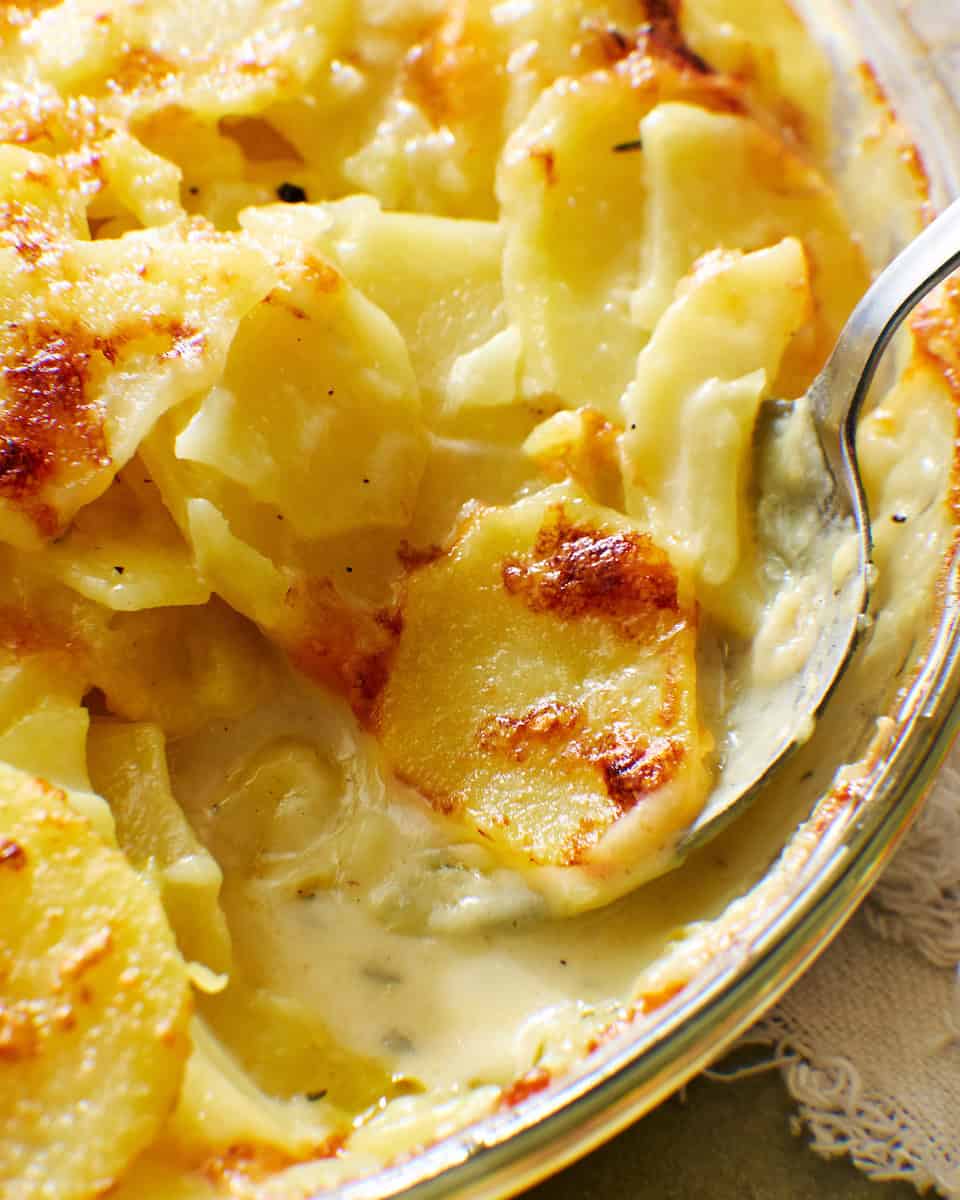 instant pot scalloped potatoes in a dish with a spoon in it, closeup on cheese sauce