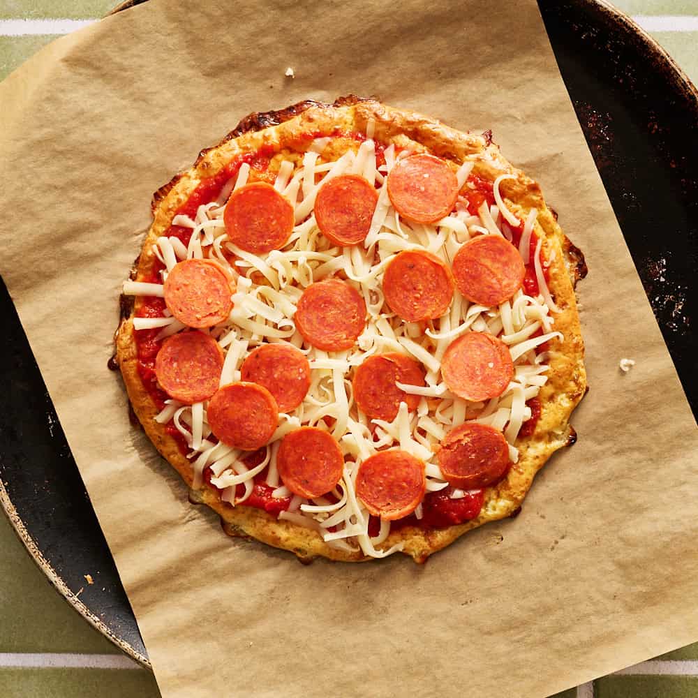 Pizza crust topped with pepperoni and cheese ready to be bakedd