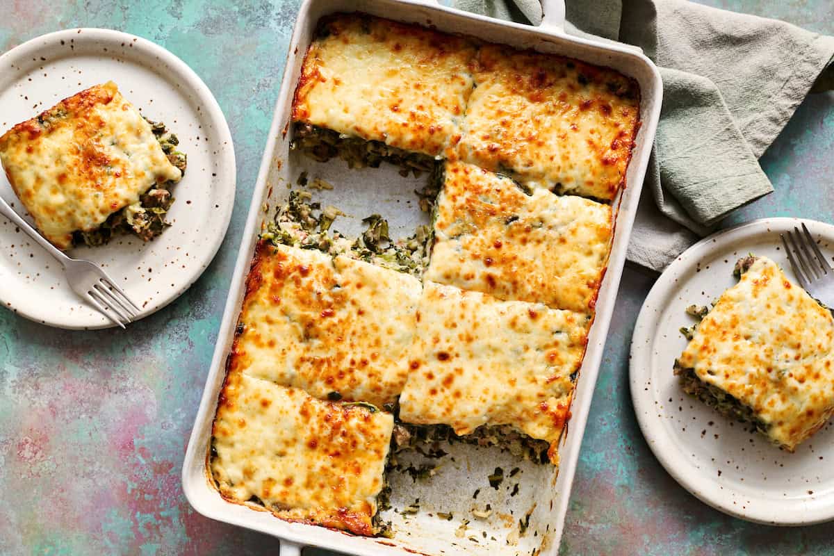 A large dish filled with a spinach, cheese and beef casserole with a piece taken out and put on a plate with a fork