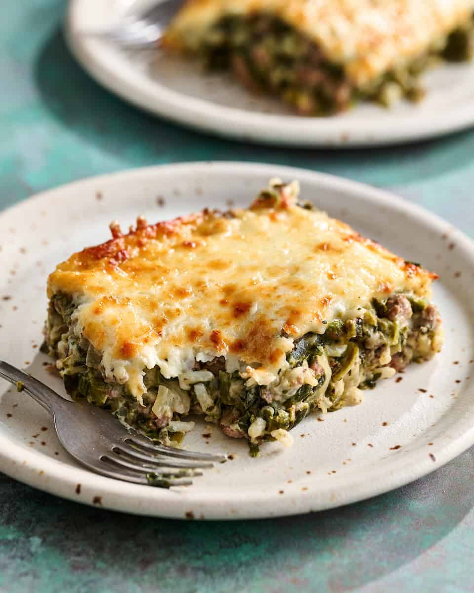 A spinach, cheese and beef casserole on a plate with a fork and a bite taken out