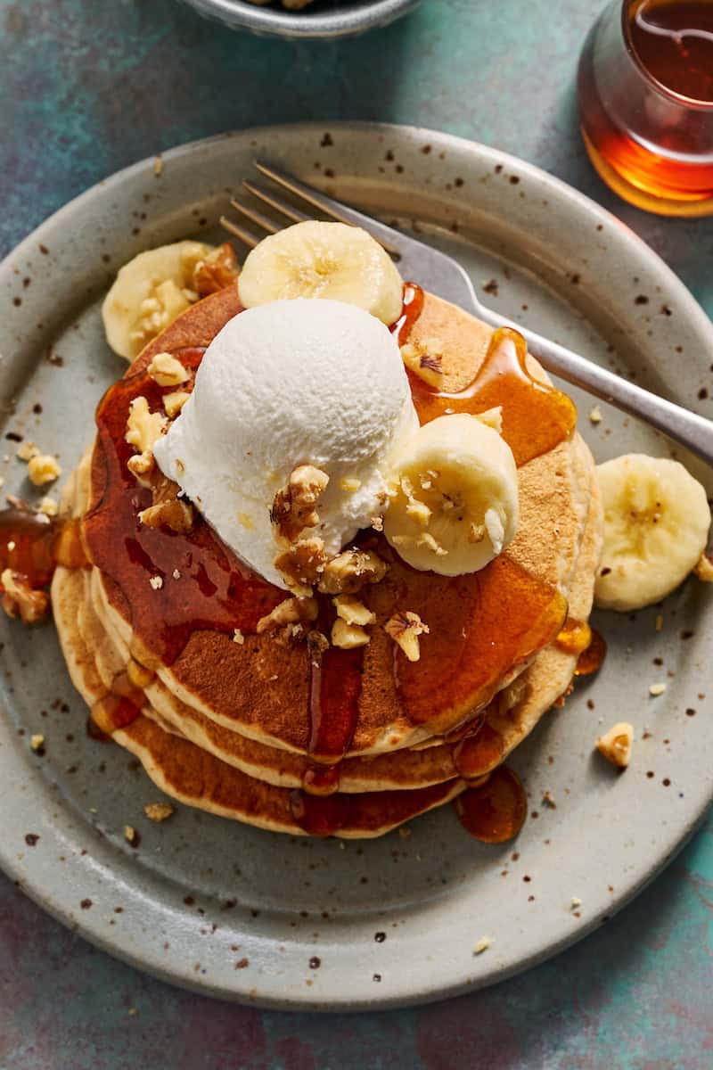 a stack of banana pancakes topped with greek yogurt, bananas and nuts