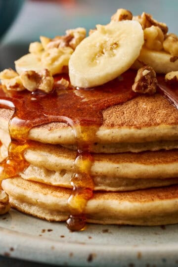 closeup of golden banana protein pancakes topped with syrup, banana and chopped walnuts