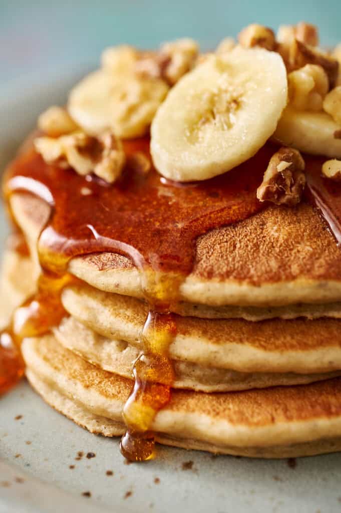 extreme closeup of golden banana protein pancakes topped with syrup, banana and chopped walnuts