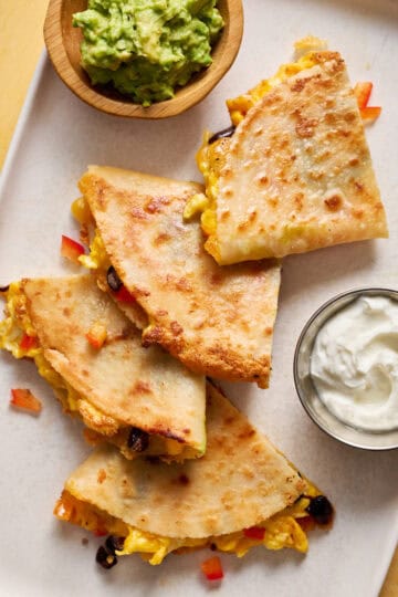 breakfast quesadillas served on a plate with greek yogurt, salsa and guac