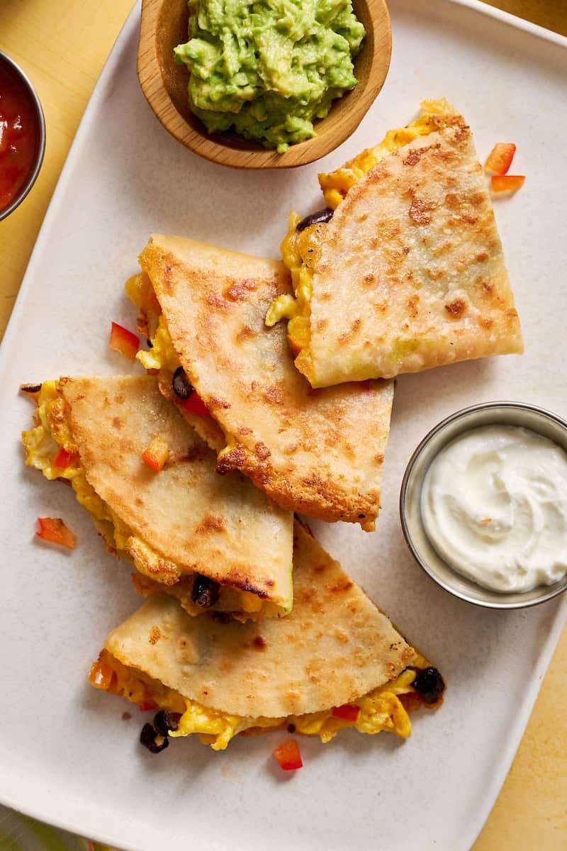 breakfast quesadillas served on a plate with greek yogurt, salsa and guac