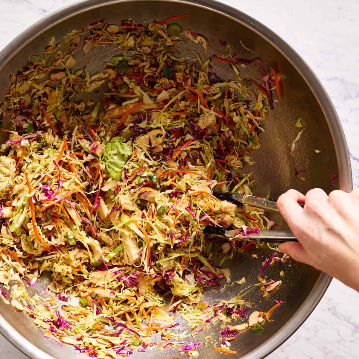 tossing ramen noodle salad in a large bowl