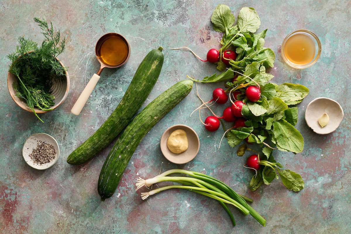 all the ingredients to make cucumber radish salad including scallions, garlic, apple cider vinegar, dijon, oil, pepper and dill