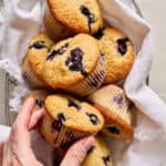 a hand reaching to take a sourdough blueberry muffin from a basket of muffins