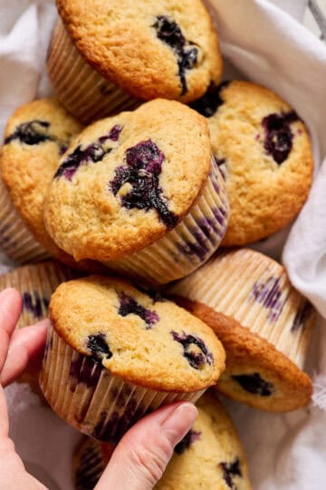 a hand reaching to take a sourdough blueberry muffin from a basket of muffins