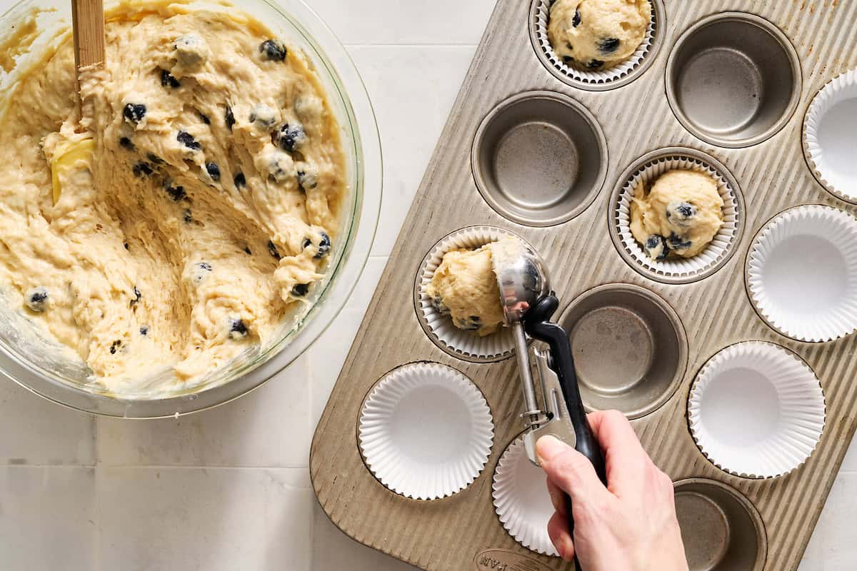scooping batter with a cookie scoop into a baking pan lined with muffin liners