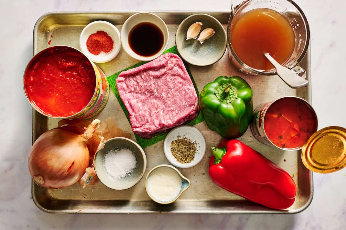ingredients to make stuffed pepper soup including peppers, tomatoes, beef, spices, garlic, onion and broth