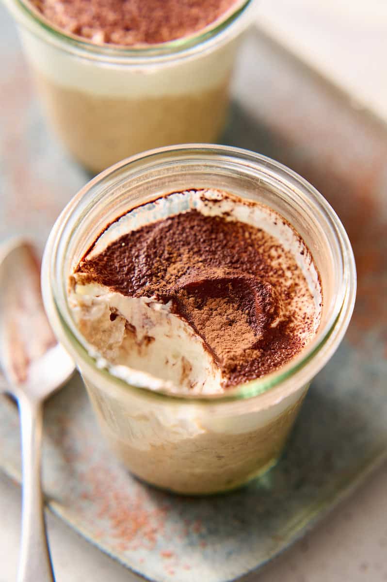 jar of tiramisu overnight oats topped with yogurt and cocoa with a spoonful taken out