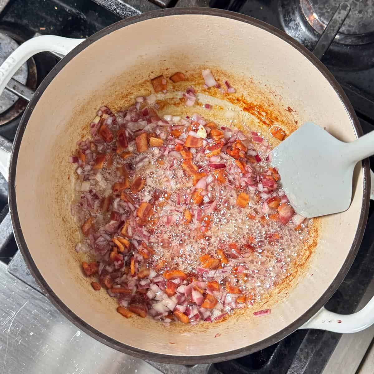 adding the red onions to the frying bacon
