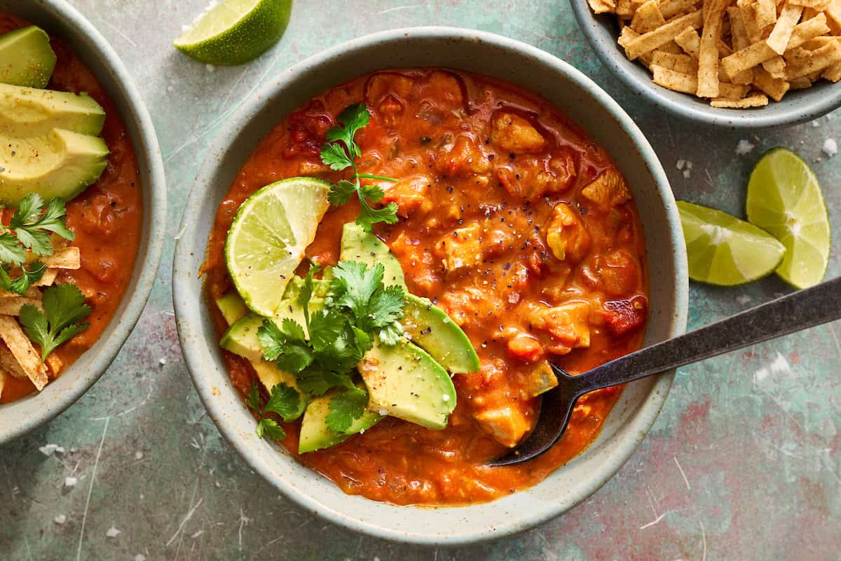 a bowl of chicken enchilada soup dressed with avocado and lime