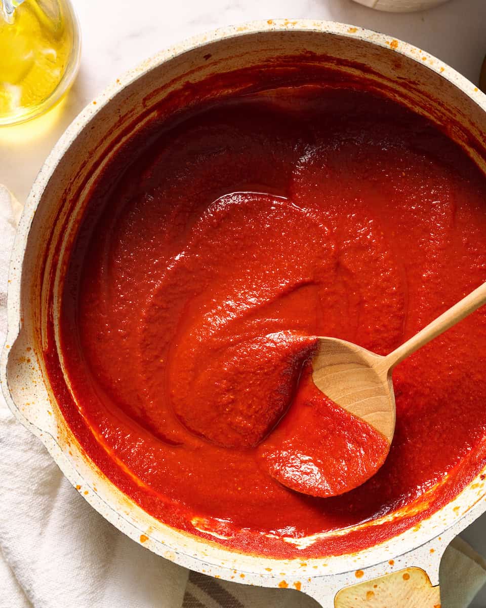 Silky red sauce in a saute pan being stirred with a wooden spoon