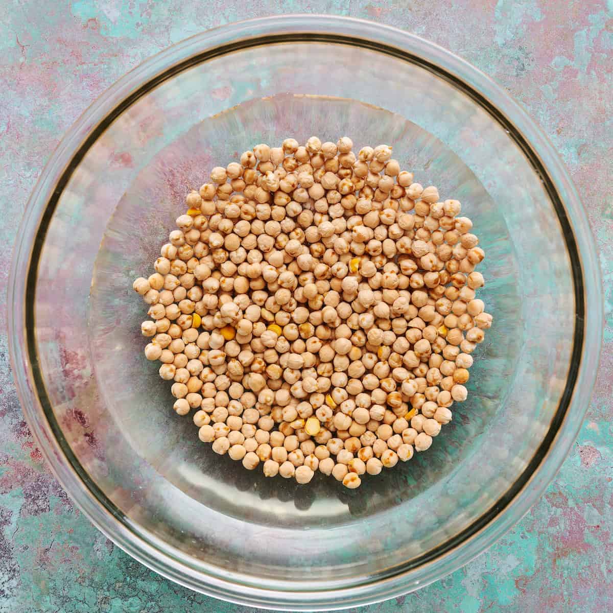 garbanzo beans soaking in a bowl with water and baking soda