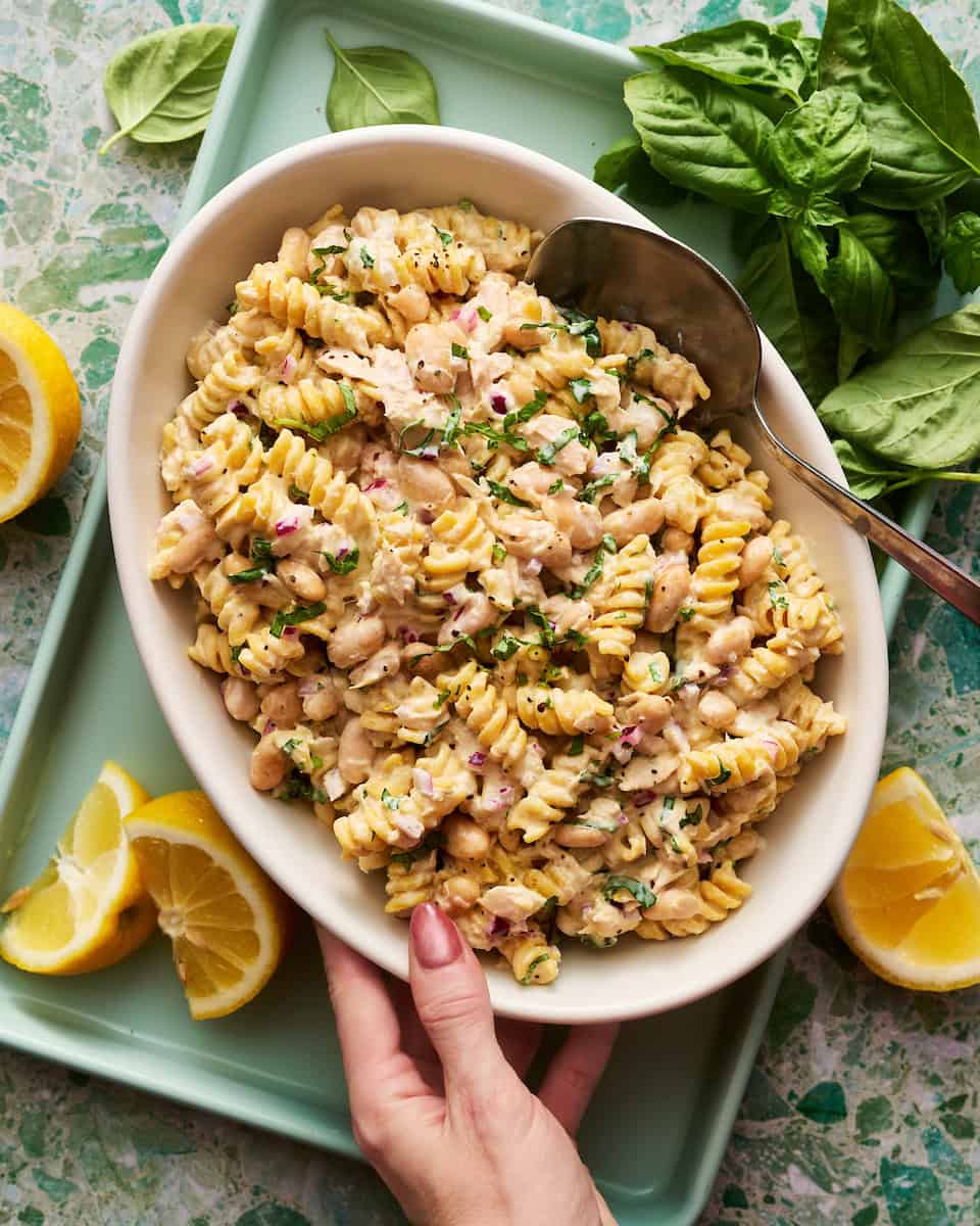 hand reaching for a bowl of pasta salad with tuna and basil
