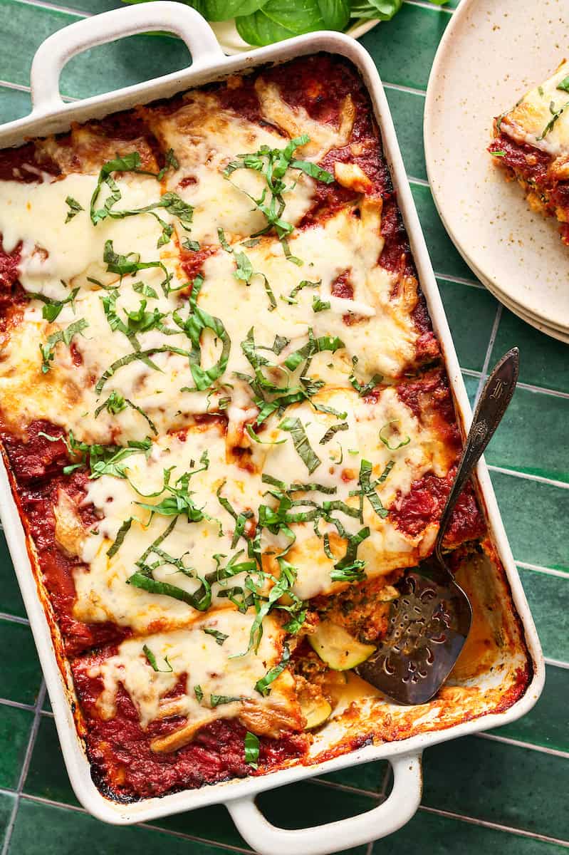 a pan of sliced zucchini lasagna topped with fresh basil