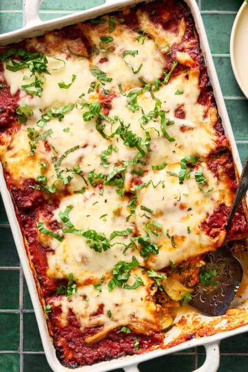 a pan of sliced zucchini lasagna topped with fresh basil
