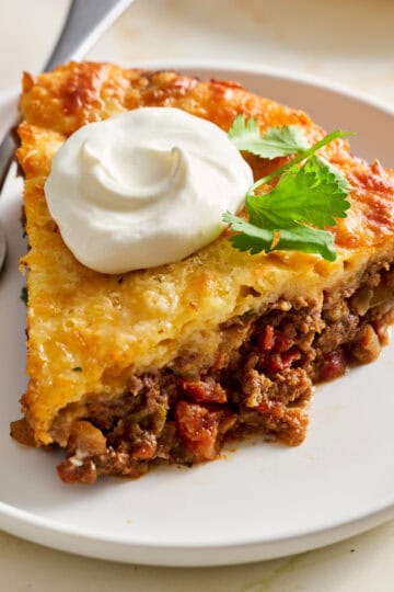 a slice of taco pie on a plate topped with cilantro and sour cream